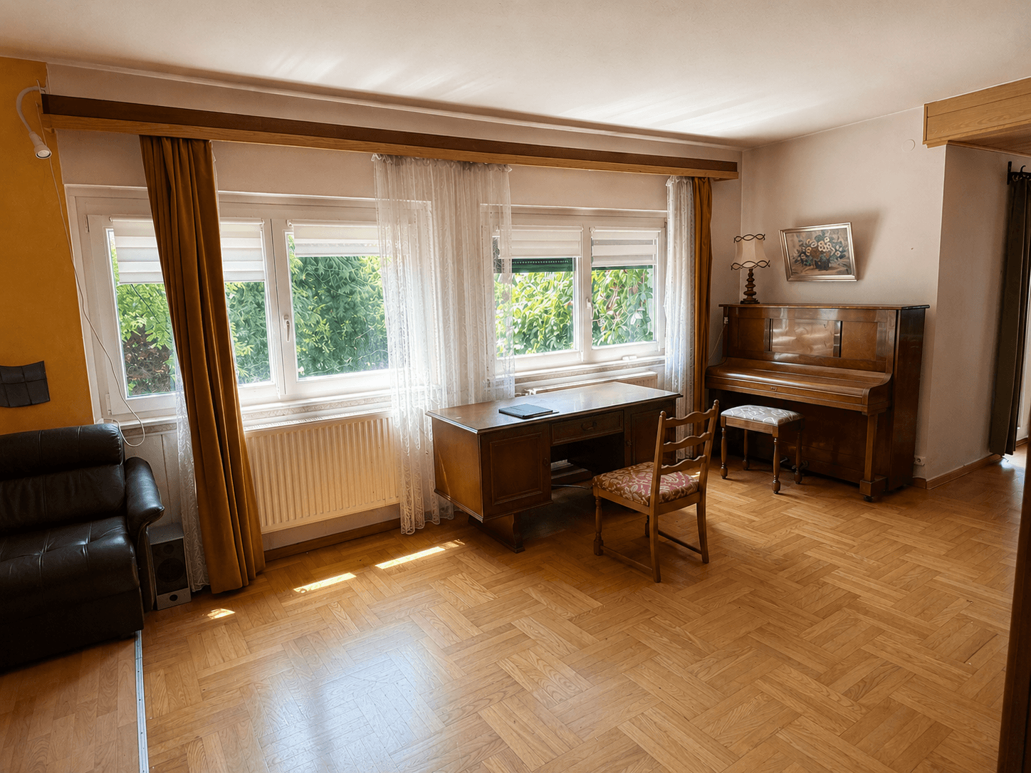 Helles Wohnzimmer mit Parkettboden, großzügigen Fenstern und einem klassischen Klavier.