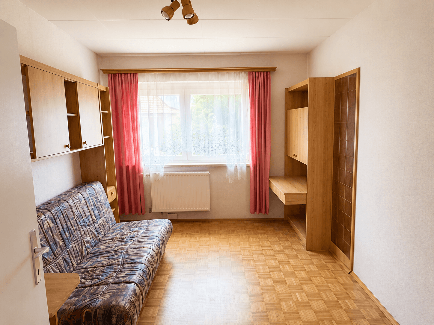 Helles Zimmer mit Parkettboden, Schlafsofa und Holzmöbeln, ideal als Gästezimmer.