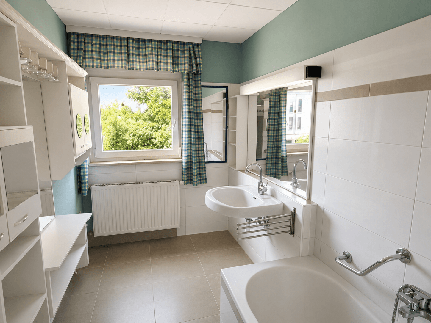 Geräumiges Badezimmer mit Badewanne, Waschbecken und Fenster, hell gefliest.