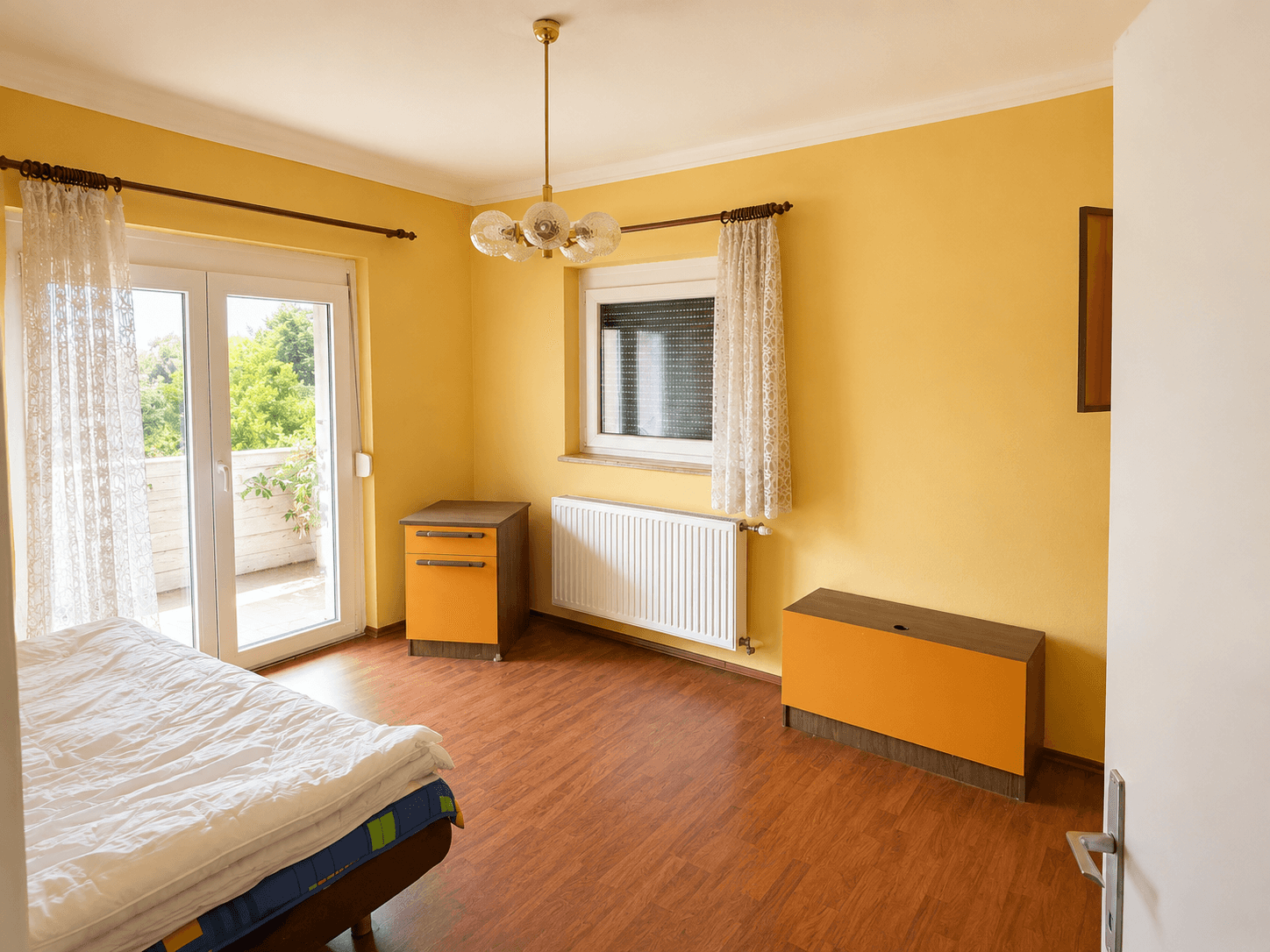 Schlafzimmer mit gelben Wänden, Holzboden und Zugang zu einem Balkon.