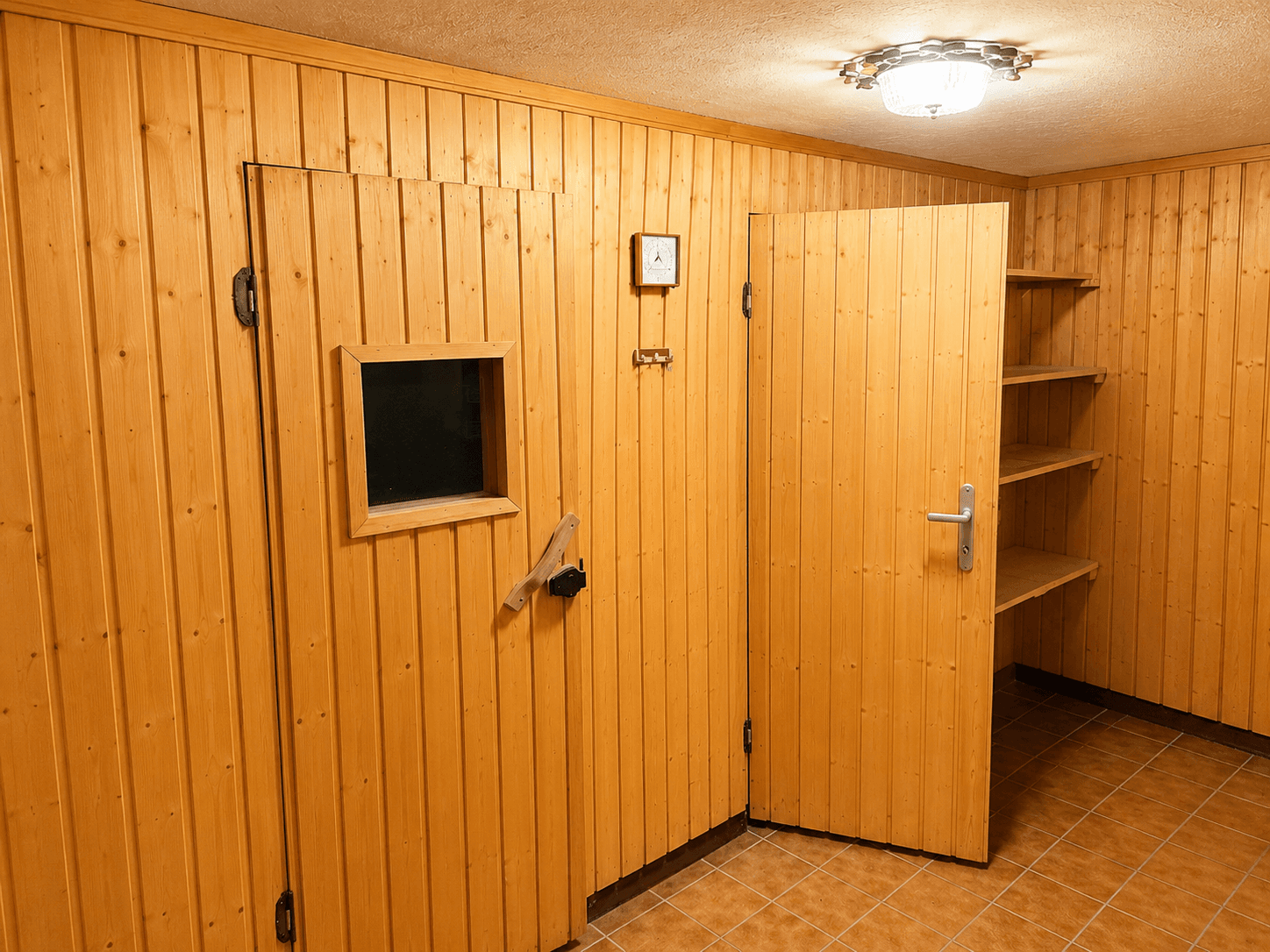 Kellerraum mit Holzverkleidung, Regalen und einer Tür zu einer Sauna oder Kühlkammer.