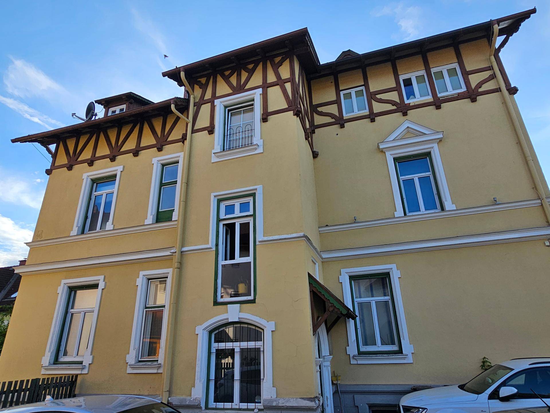 Vorderansicht der gelben Villa mit Eingangsbereich und dekorativen Fensterrahmen.