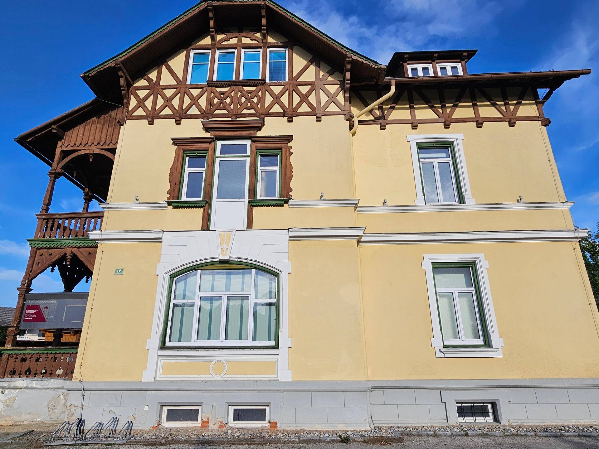Fassade der gelben Villa mit großen Fenstern und dekorativen Holzelementen.