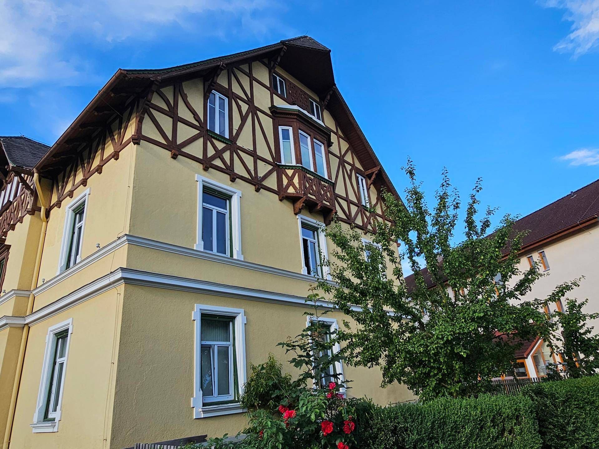Ansicht der gelben Villa mit Erkerfenster und gepflegter Bepflanzung im Vorgarten.