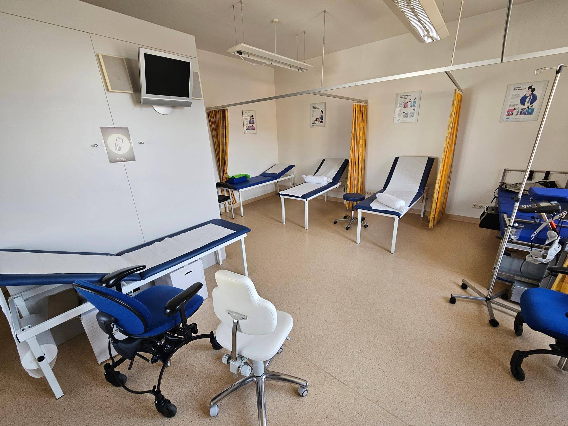 Behandlungszimmer mit Untersuchungsliege, Bürostühlen und Zugang zum Balkon.
