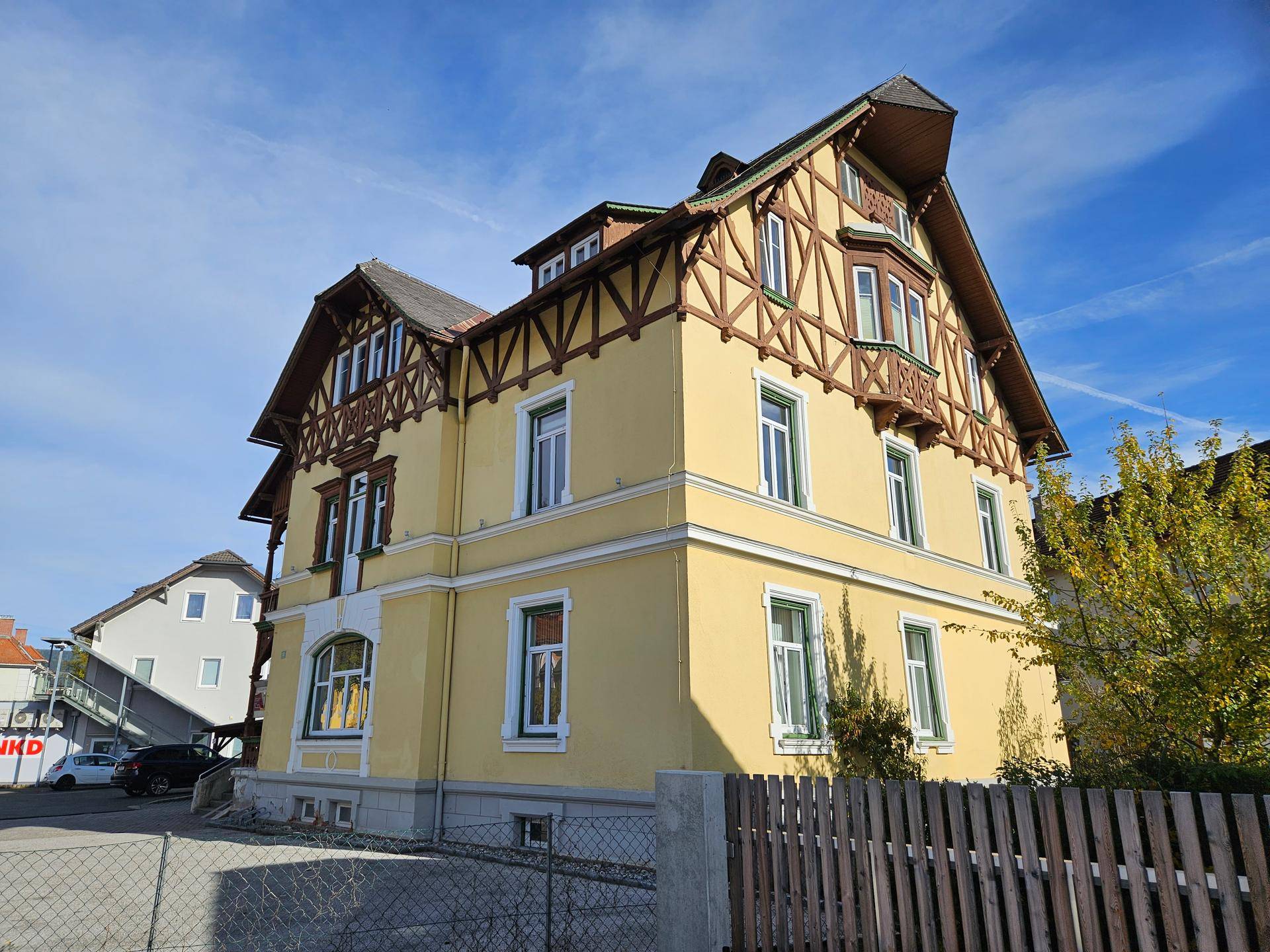 Seitenansicht der gelben Villa mit Fachwerk und Holzzaun im Vordergrund.