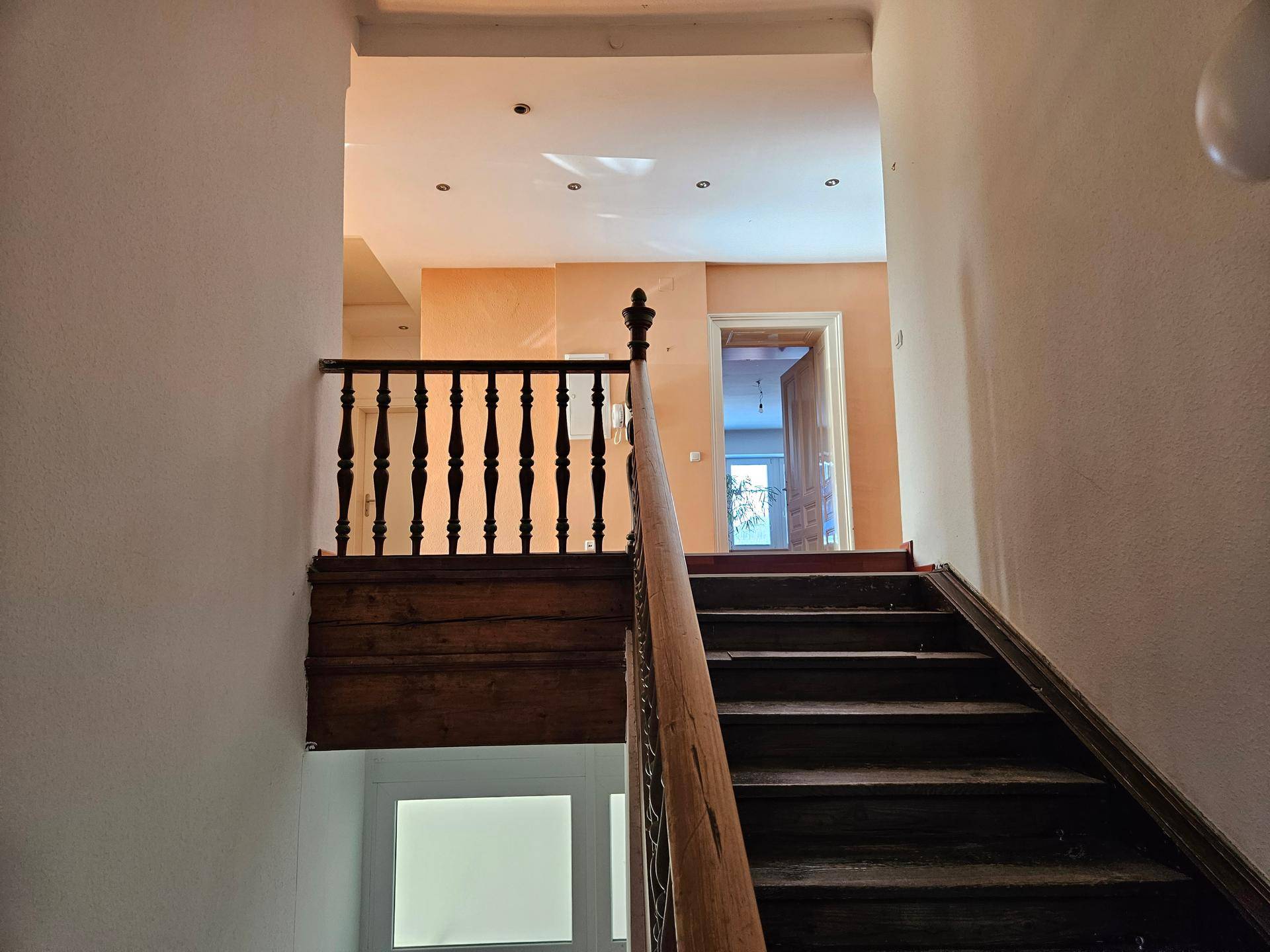 Detailansicht der Holztreppe mit kunstvollem Geländer und Blick auf den oberen Bereich.