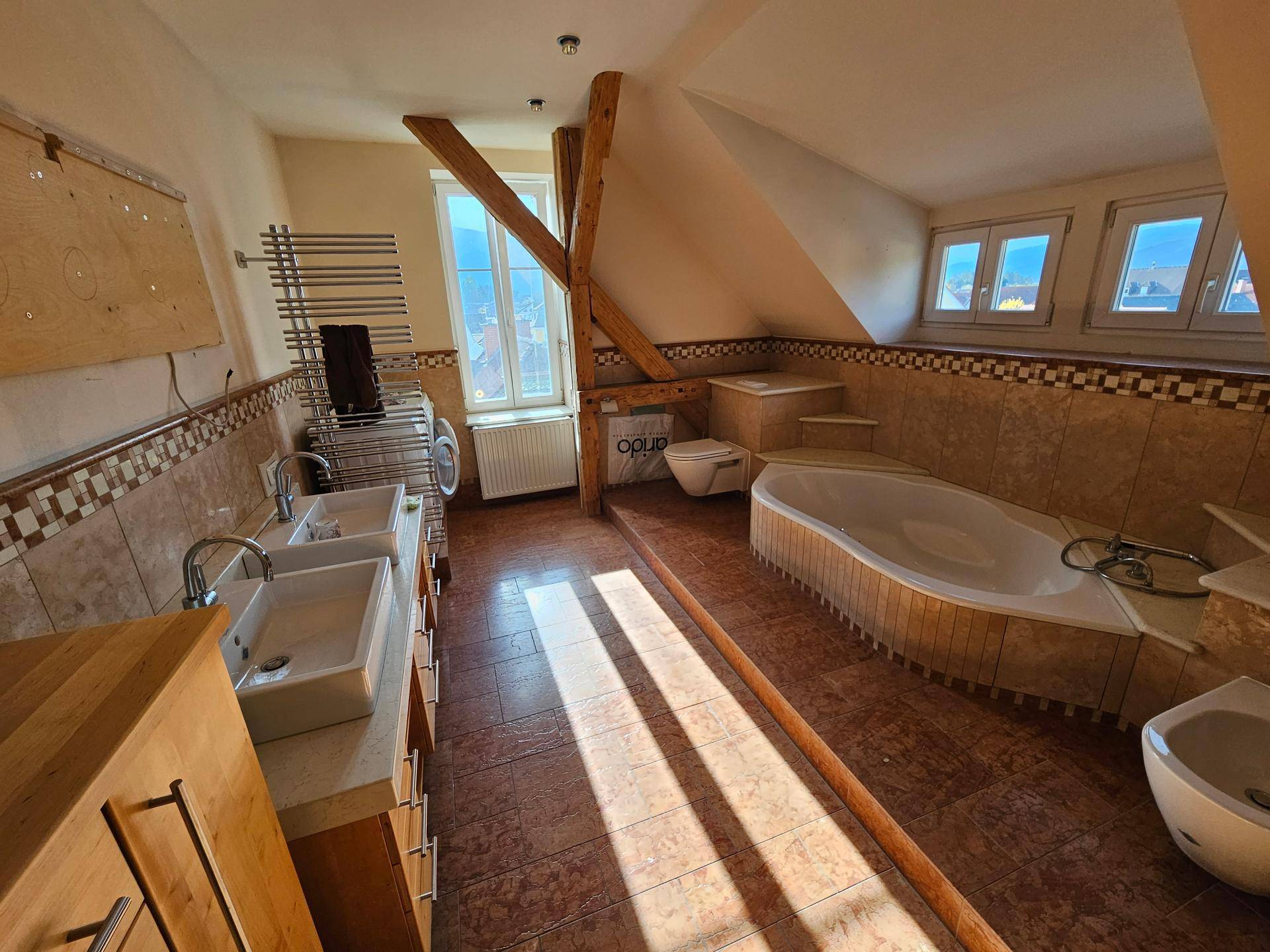 Großes Badezimmer mit Fliesenboden, Badewanne, Doppelwaschbecken und sichtbaren Holzbalken.