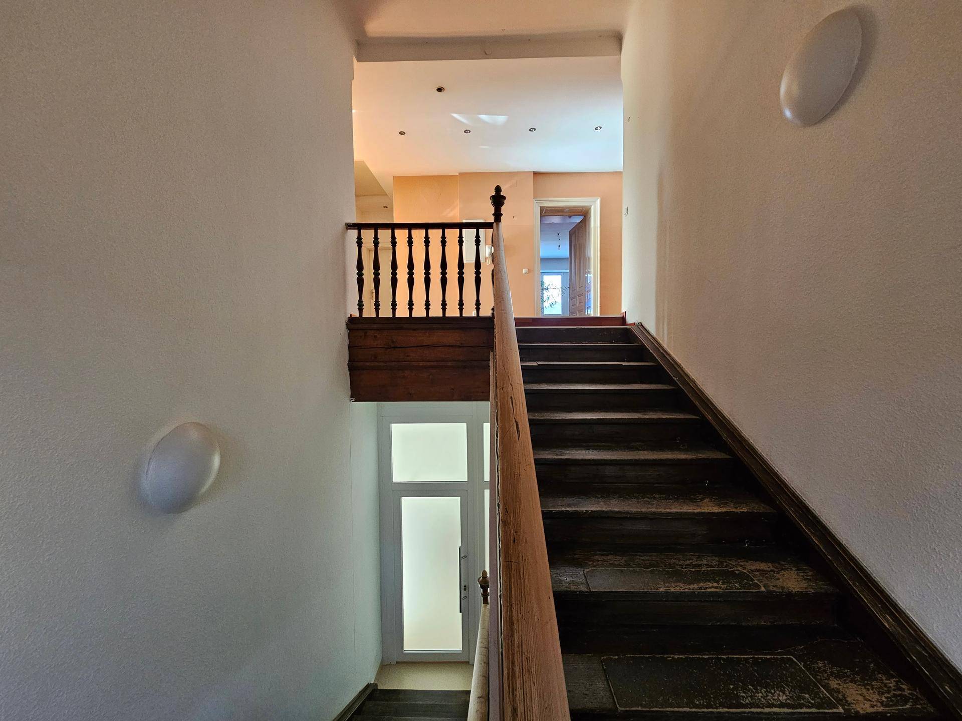 Blick auf eine Holztreppe mit gedrechseltem Geländer, die zu einem oberen Flur führt.