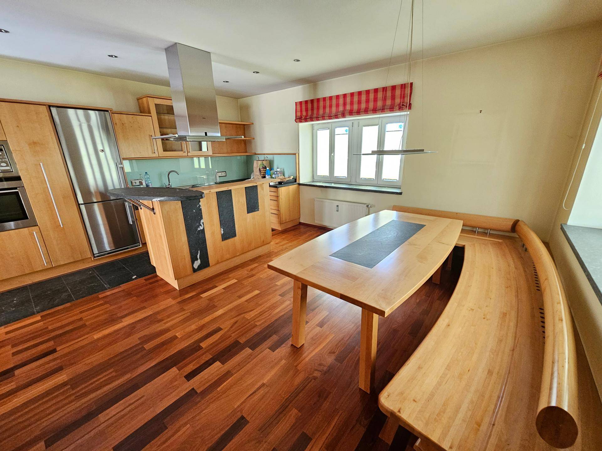 Moderne Holzküche mit Edelstahlelementen, Kochinsel und einem gemütlichen Essbereich mit Holzbänken.
