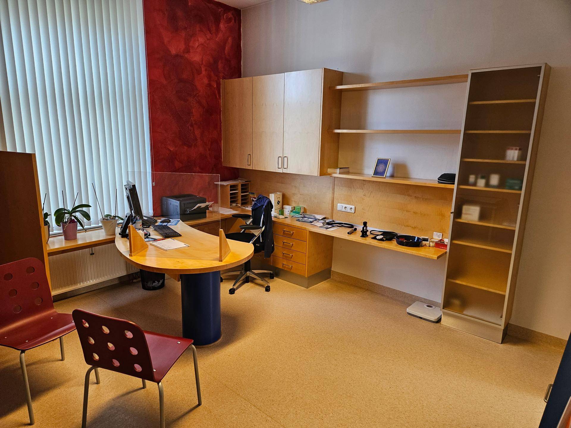 Beratungszimmer mit Schreibtisch, Bürostuhl und roter Akzentwand.