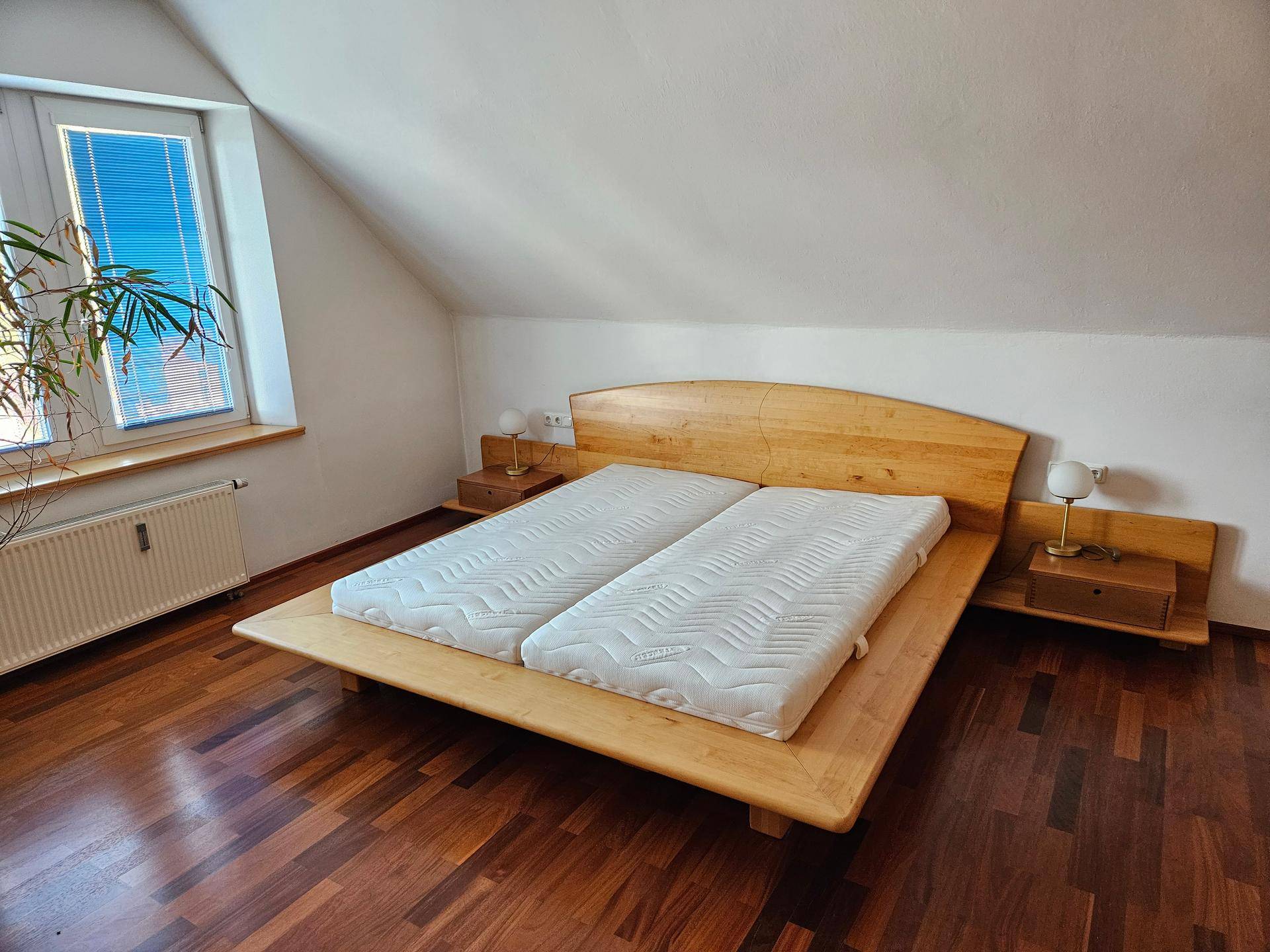 Helles Schlafzimmer mit Holzbett, Nachttischen, Holzboden und schräger Decke.