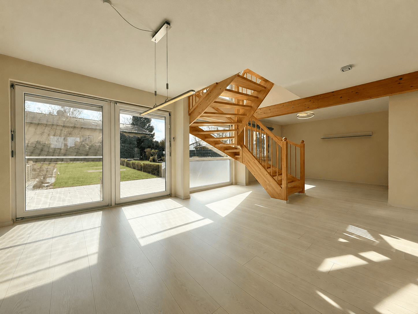 Helles Wohnzimmer mit Holztreppe, Parkettboden und großen Fenstern mit Zugang zum Garten.