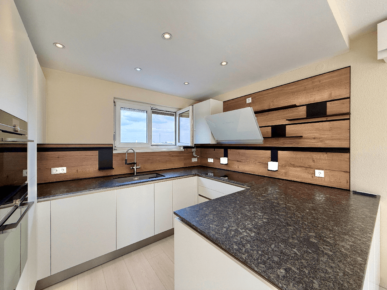 Moderne Küche mit weißen Hochglanzfronten, dunkler Granitarbeitsplatte und Holzakzenten an der Wand.