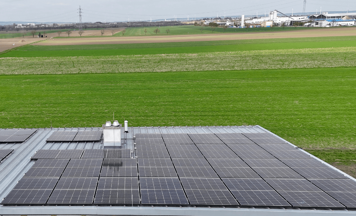 Dach eines Gebäudes mit Photovoltaikanlage und weitem Blick über grüne Felder und die Landschaft.