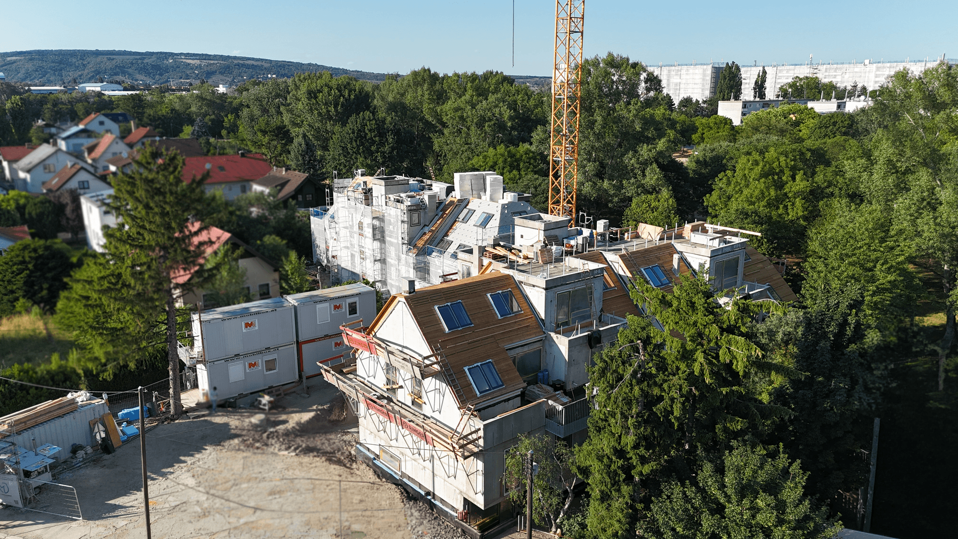 Luftaufnahme einer Baustelle mit im Bau befindlichen Gebäuden und Kran im Grünen.