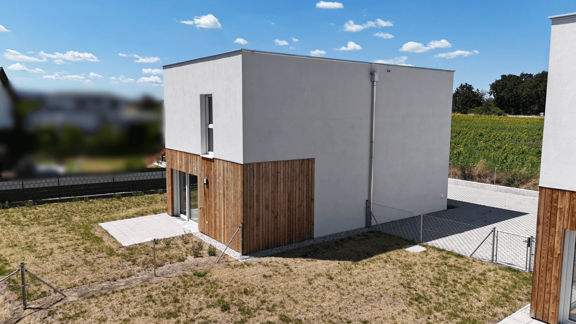 Neubau-Einfamilienhaus mit weißer Fassade und Holzelementen, angrenzend an weite Felder.