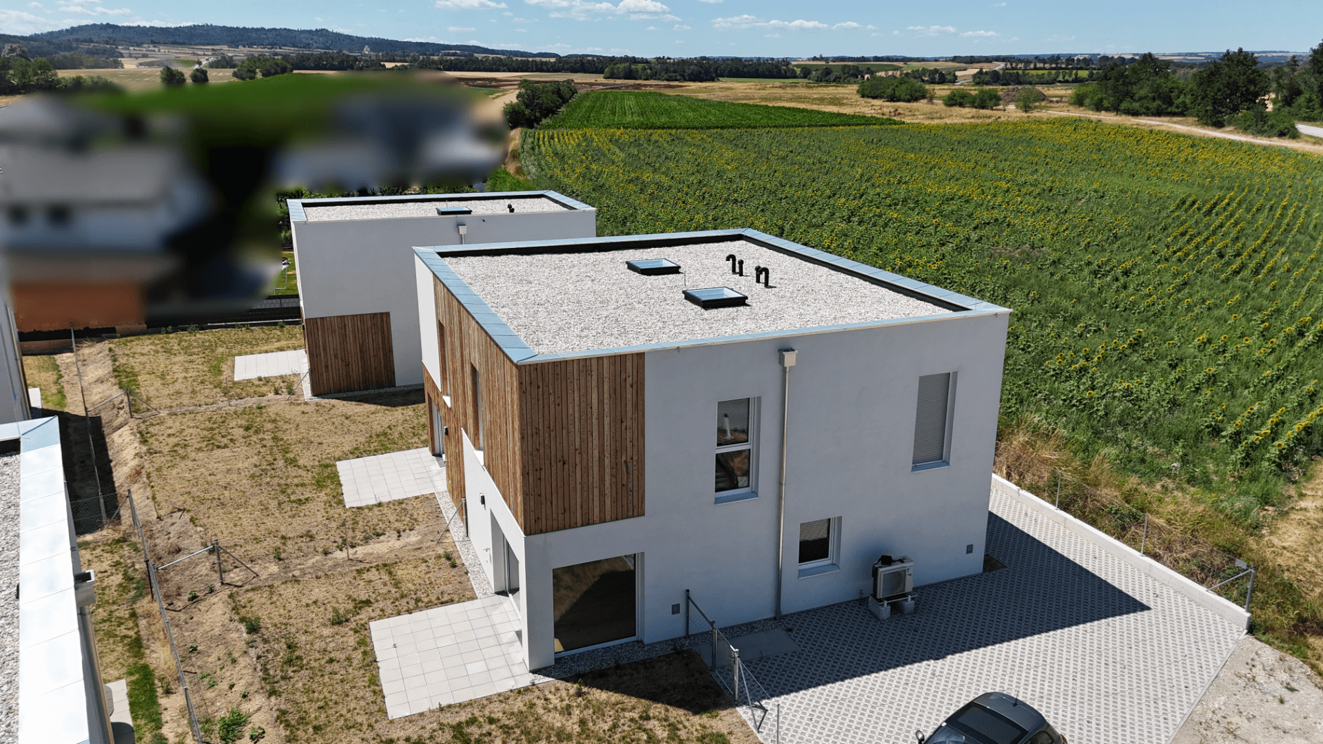 Neubau-Reihenhäuser mit Flachdach und Holzfassaden, umgeben von Feldern unter blauem Himmel.