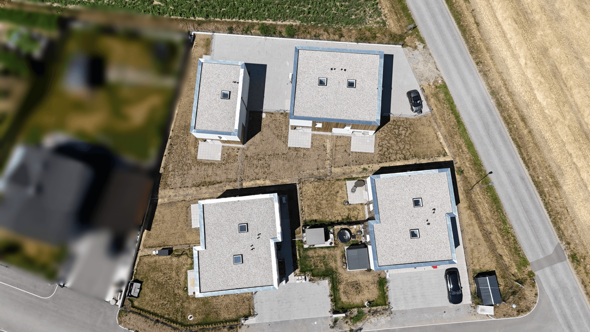 Vogelperspektive von vier modernen Einfamilienhäusern mit Flachdächern und angrenzenden Parkplätzen.