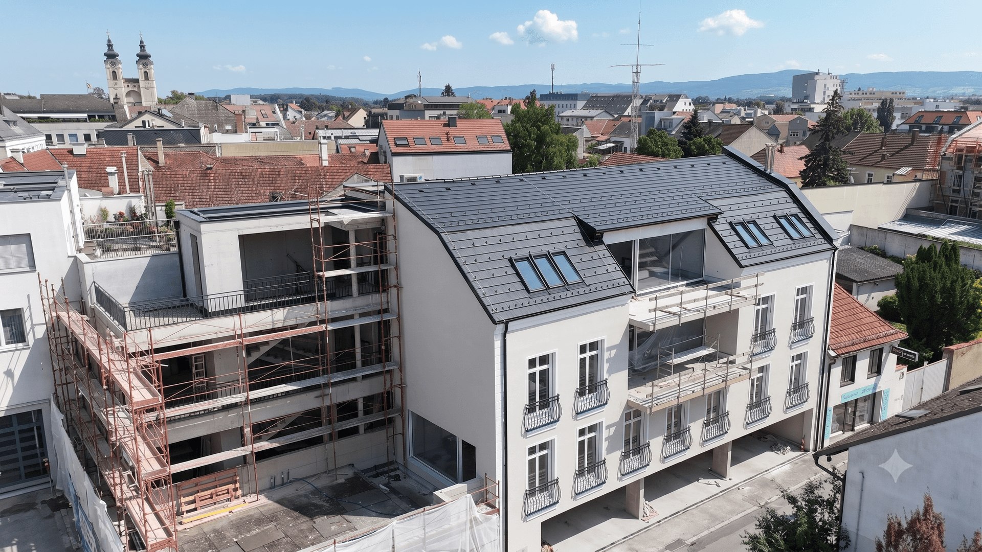 Moderner Neubau in der Bauphase mit Blick auf die Stadt und Kirchtürme, helle Fassade.