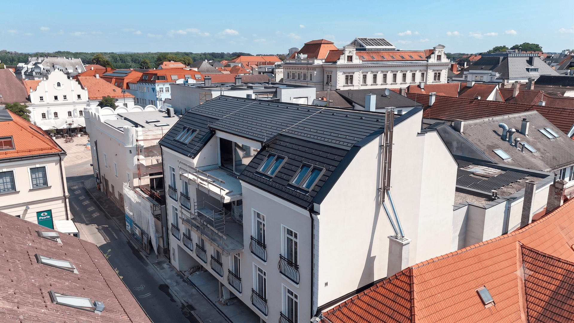 Luftaufnahme des Neubaus in der Stadt, umgeben von traditionellen Dächern, mit modernen Elementen.