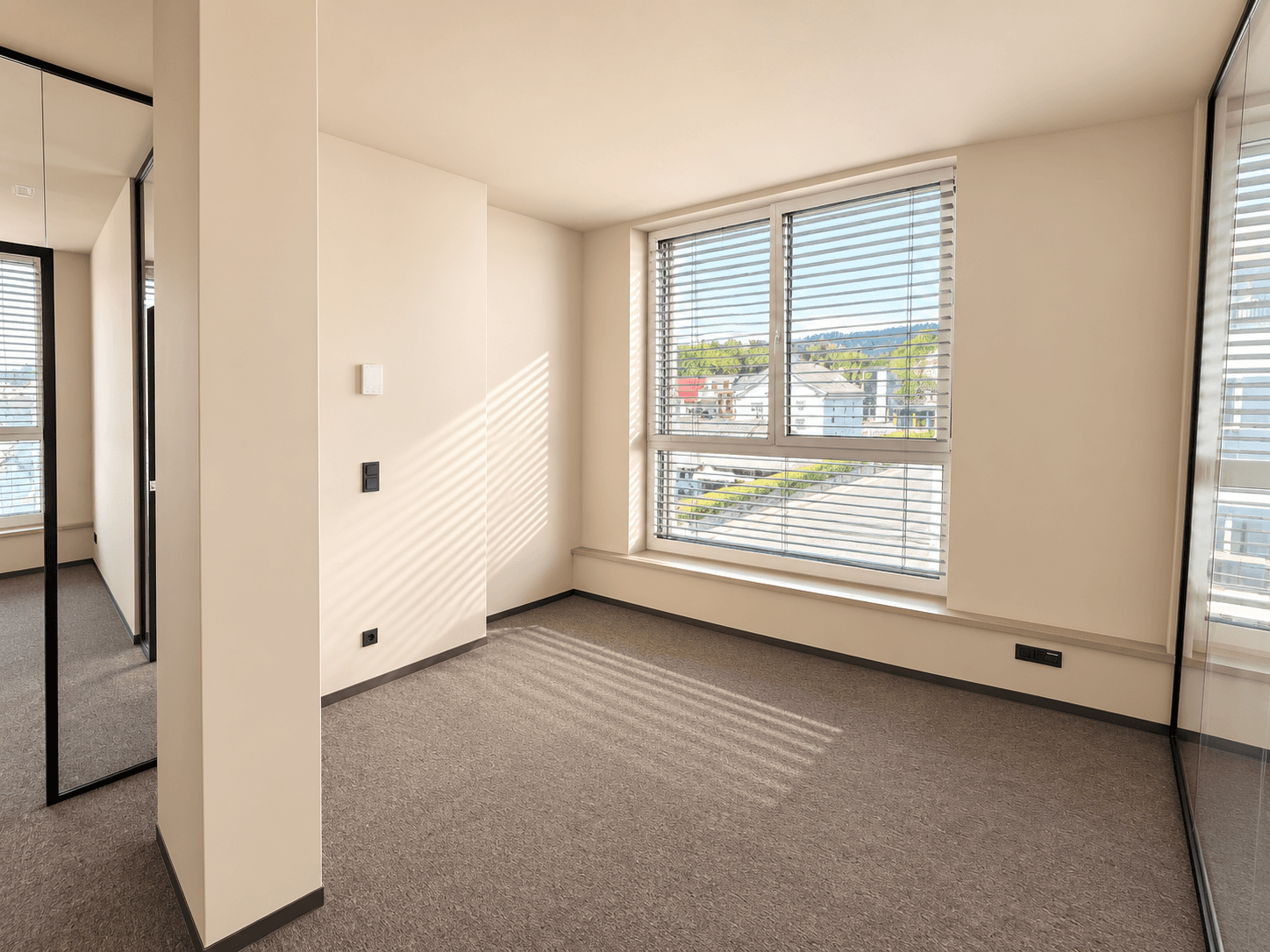 Geräumiger Büroraum mit Teppichboden und einem großen Fenster, das einen Blick auf die Straße ermöglicht.
