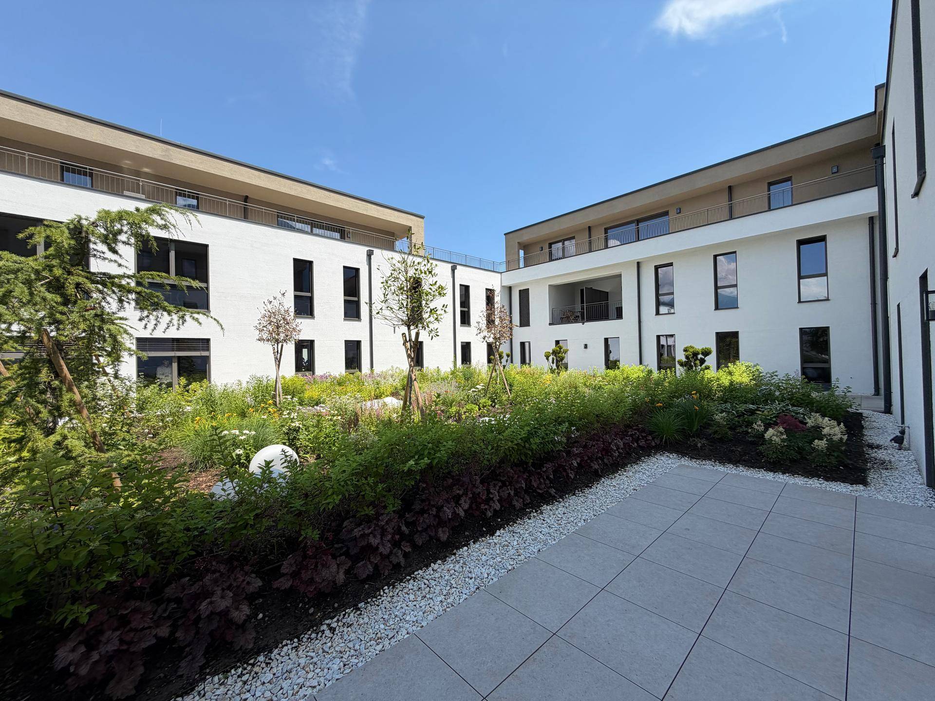 Moderner Gebäudekomplex mit weißer Fassade und einem schön angelegten Innenhof mit viel Grün.