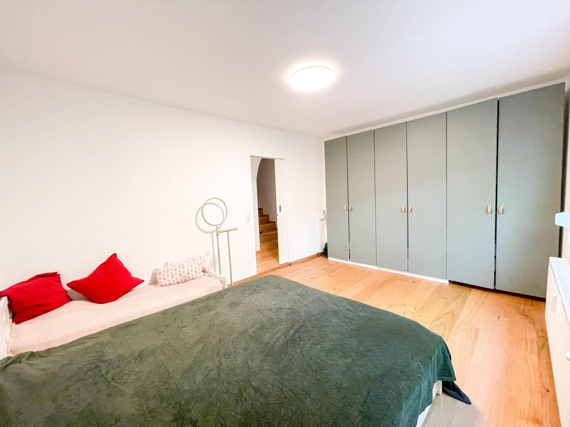 Geräumiges Schlafzimmer mit durchgehenden Einbauschränken, Holzboden und Zugang zu einem weiteren Bereich.