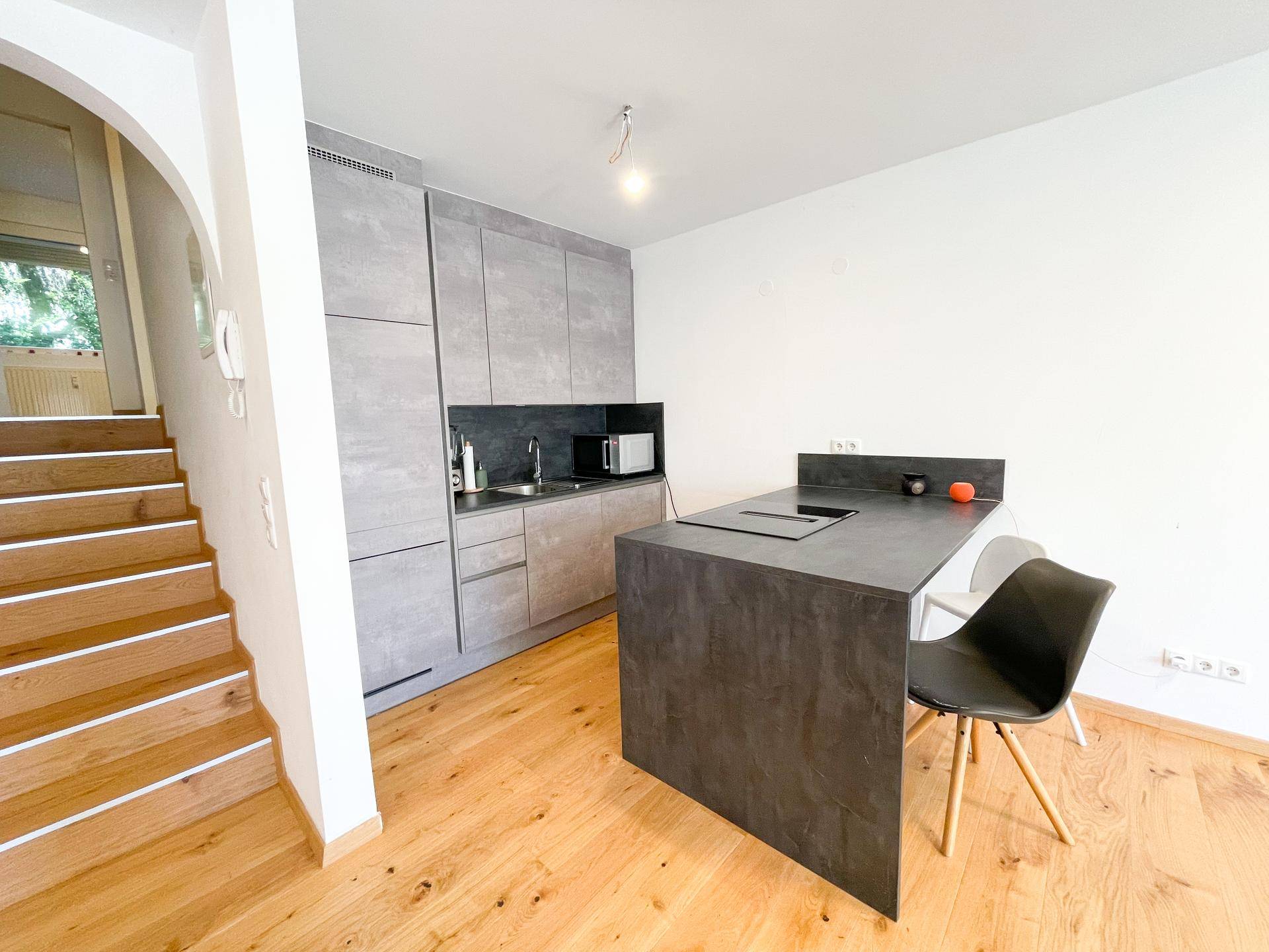 Moderne Küche mit grauen Schränken, Kücheninsel und integriertem Kochfeld neben der Holztreppe.