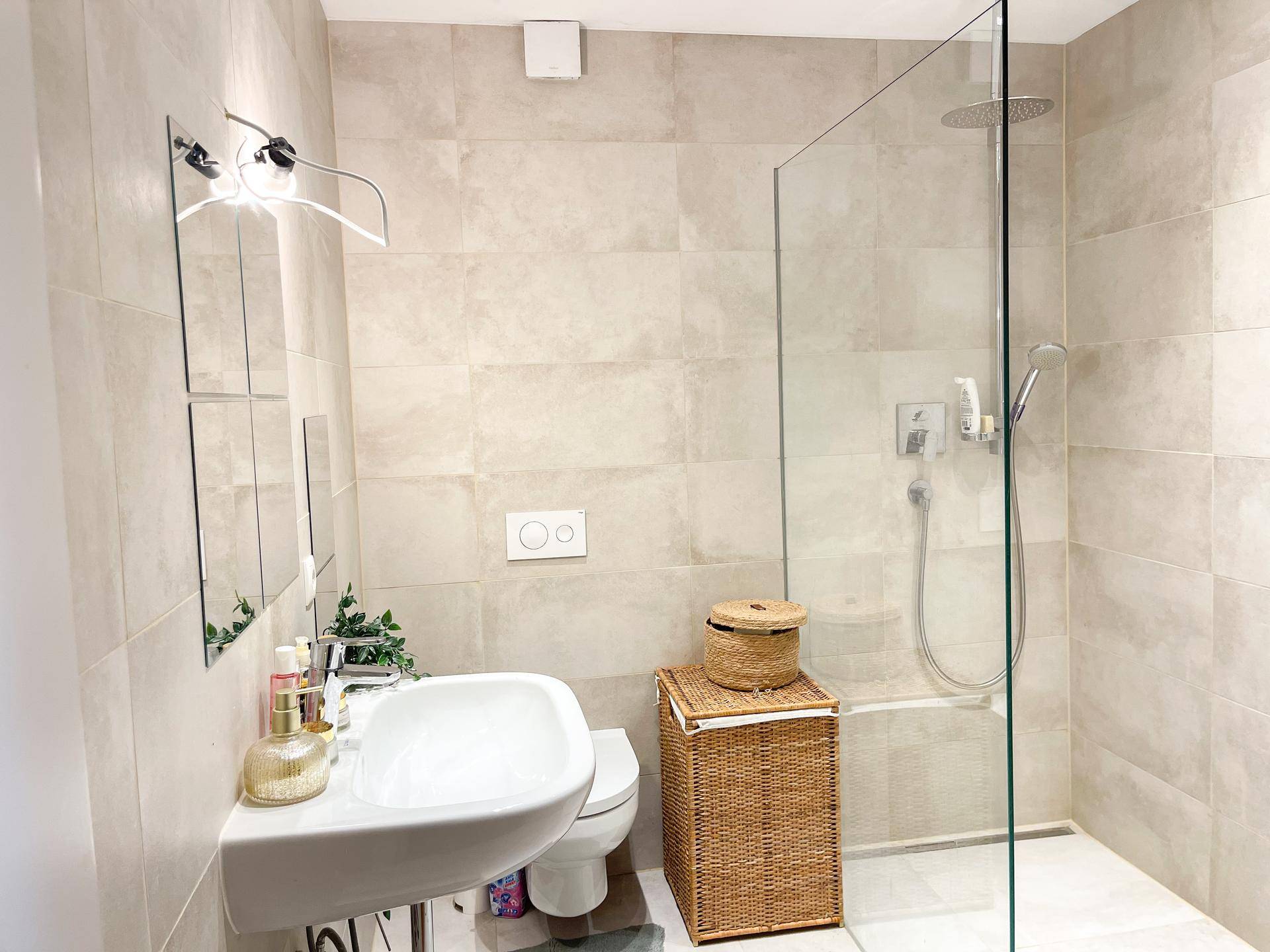 Modernes Badezimmer mit beigen Fliesen, ebenerdiger Dusche und wandhängendem WC.