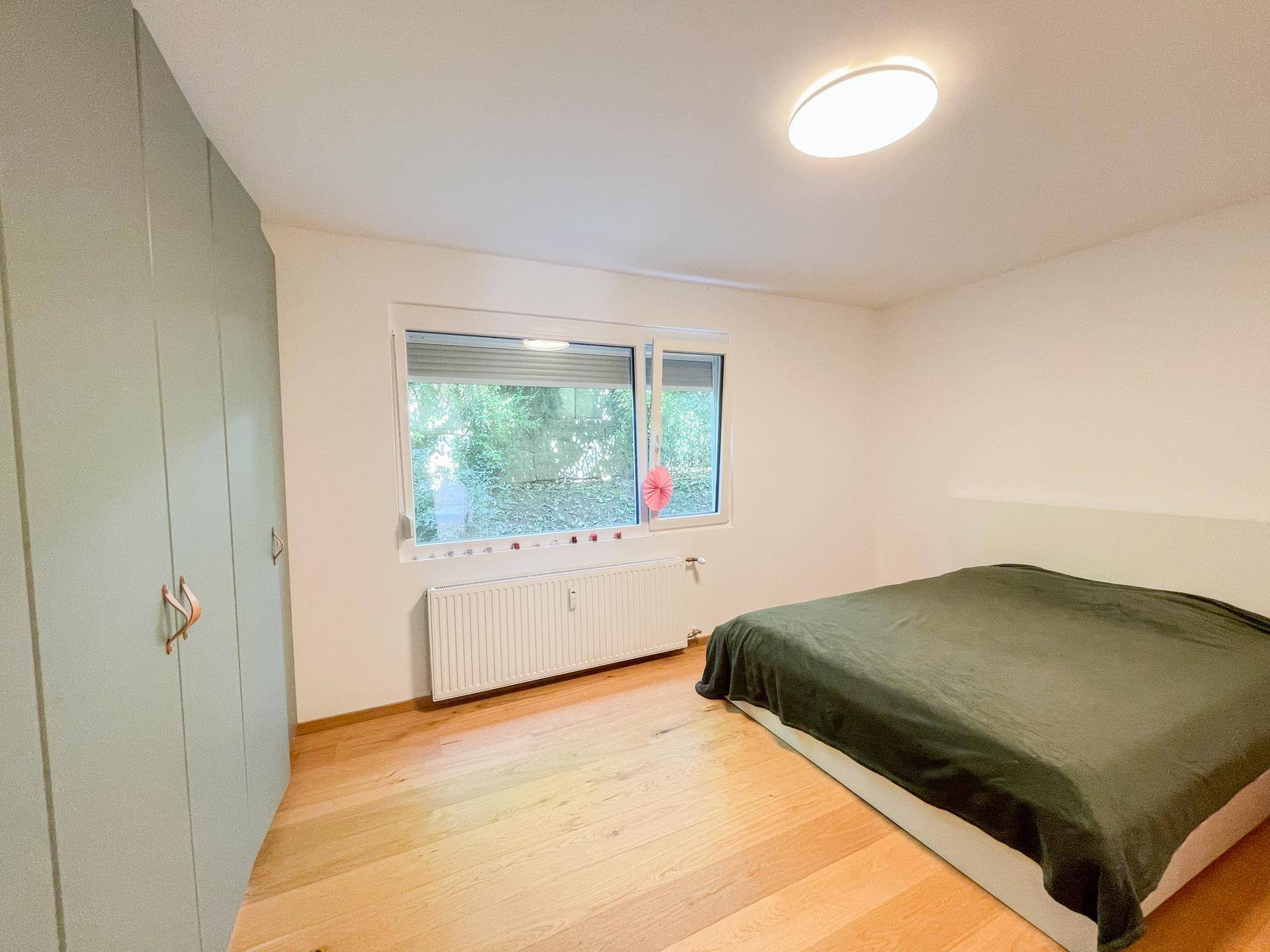 Helles Schlafzimmer mit Holzboden, großem Fenster und praktischen Einbauschränken.