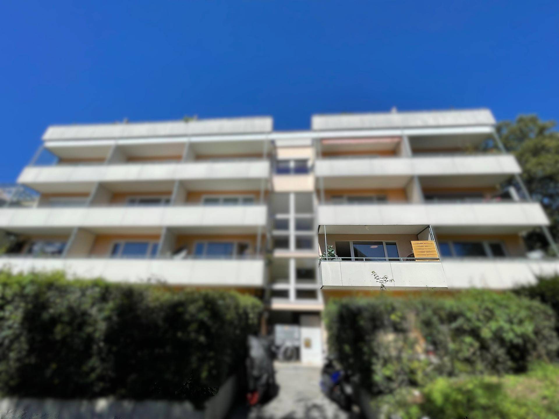 Mehrstöckiges Apartmentgebäude mit zahlreichen Balkonen und grüner Hecke im Vordergrund.