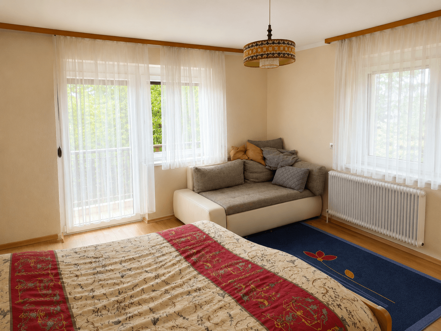 Helles Schlafzimmer mit Balkonzugang, Sofa und Blick ins Grüne.