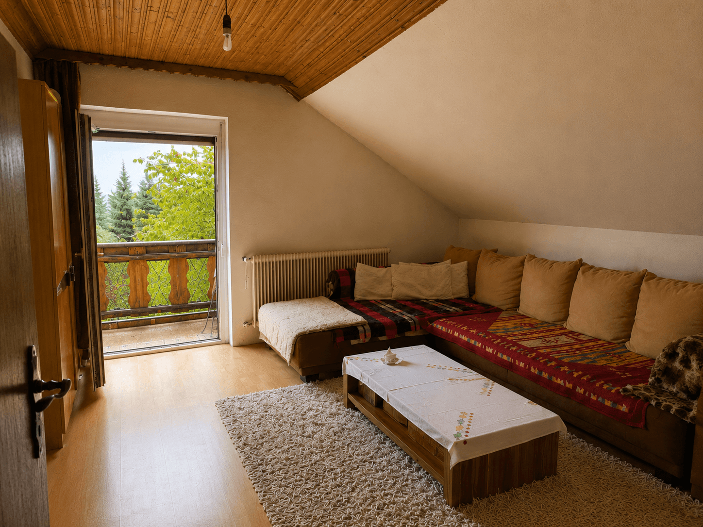 Gemütliches Wohnzimmer im Dachgeschoss mit Balkonzugang und Holzbalkendecke.