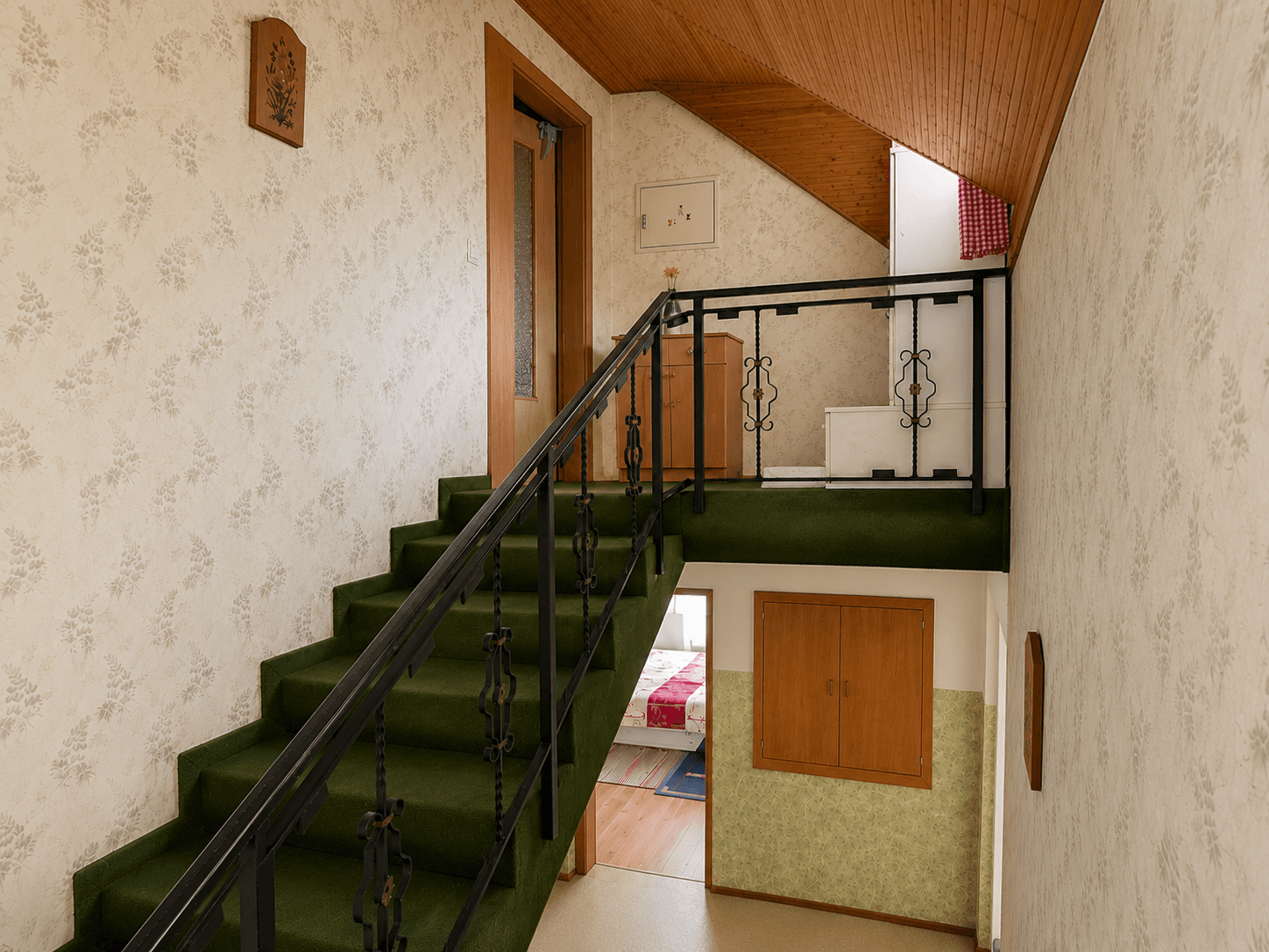 Treppenhaus mit grünem Teppichboden, gemusterter Tapete und Holzdecke.