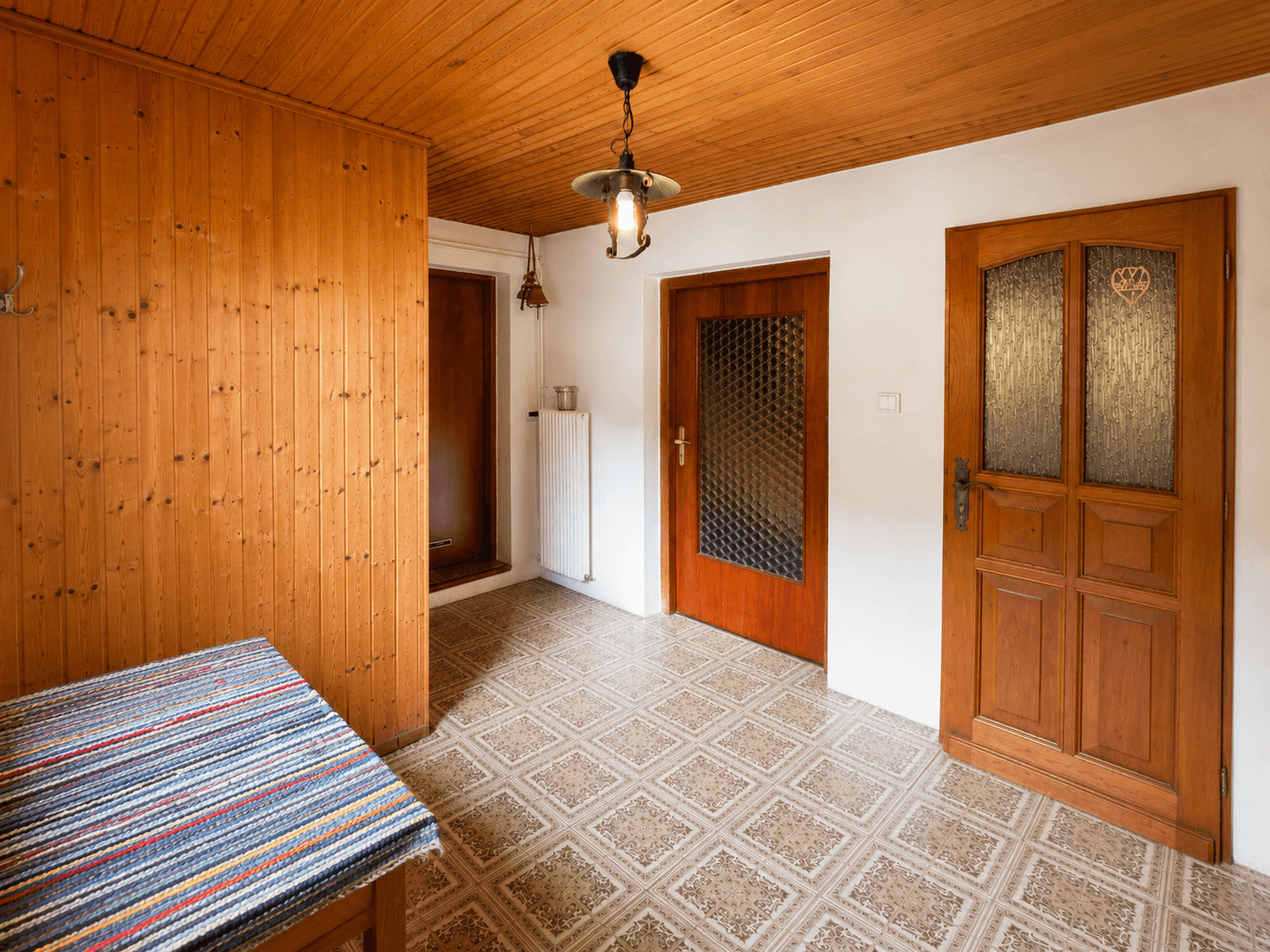 Eingangsbereich mit Holztäfelung, gemustertem Fliesenboden und Holztüren.