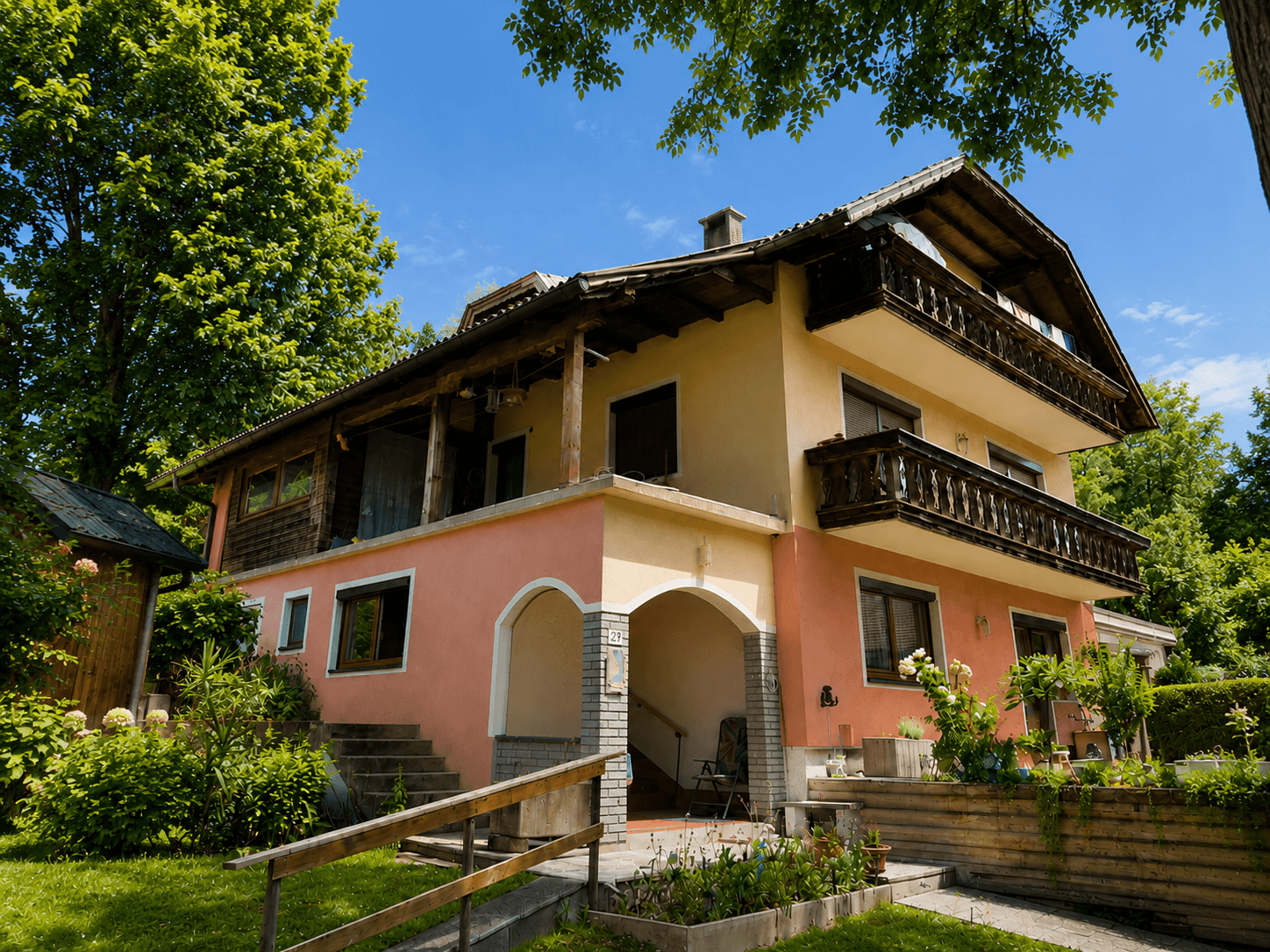 Charmantes Haus mit mehreren Balkonen und gepflegtem Vorgarten unter blauem Himmel.