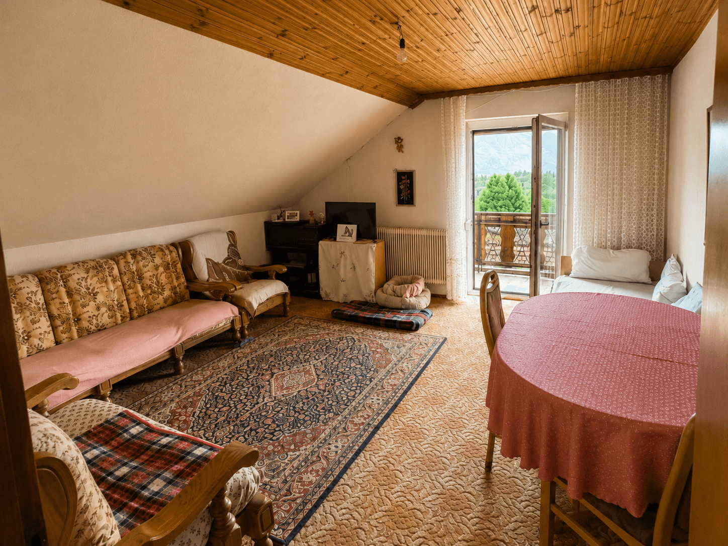 Geräumiges Dachgeschoss-Wohnzimmer mit traditionellen Möbeln und Balkonblick.