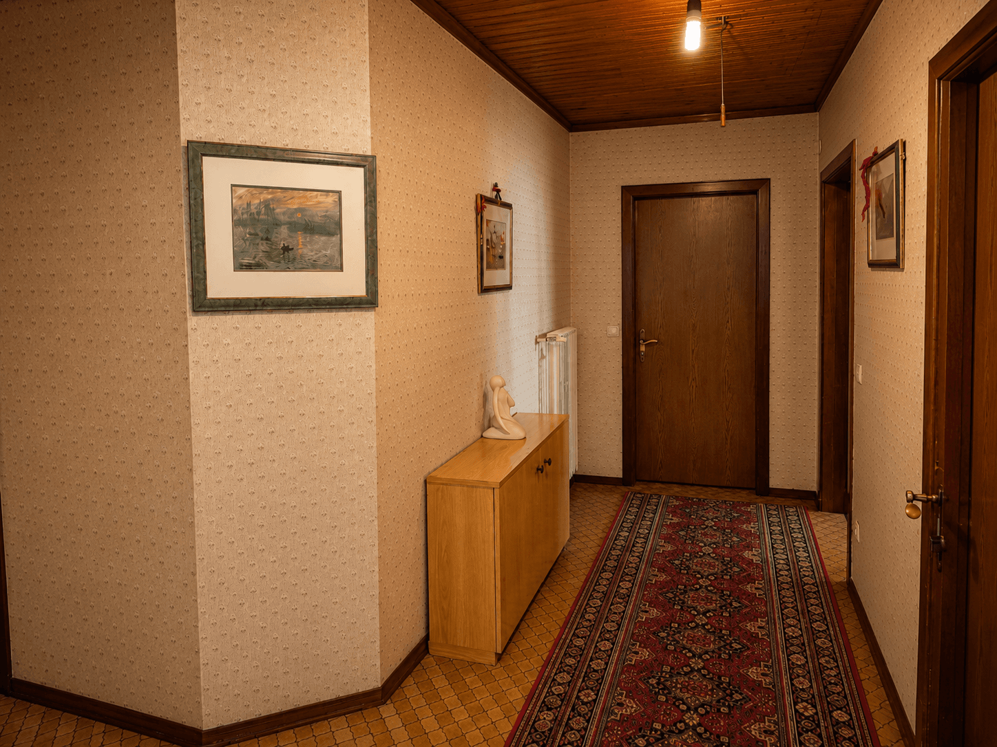 Flur mit gemusterter Tapete, Holzdecke und traditionellem Teppichläufer.