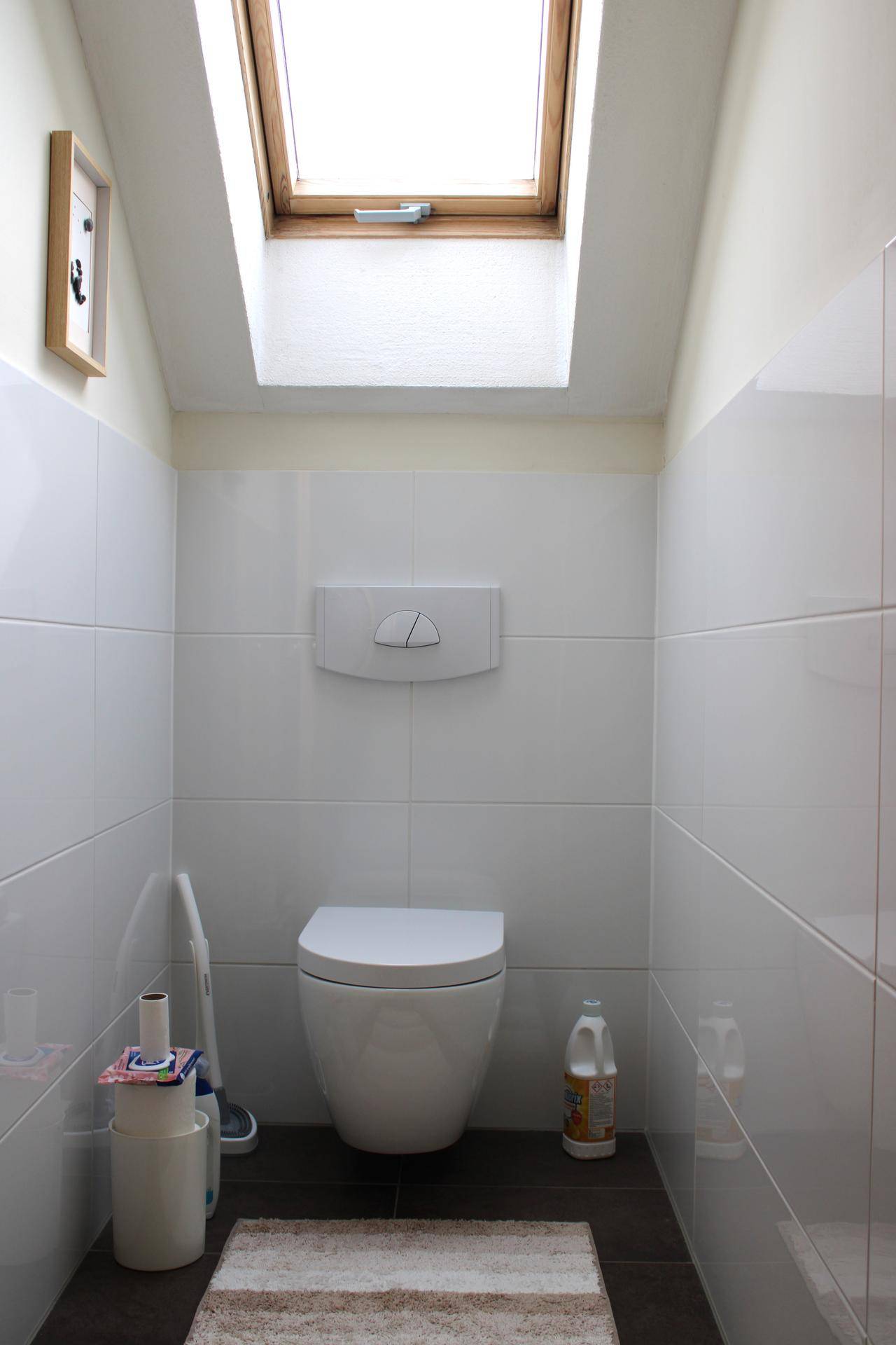 Modernes Gäste-WC mit wandhängender Toilette, weißen Fliesen und Dachfenster.