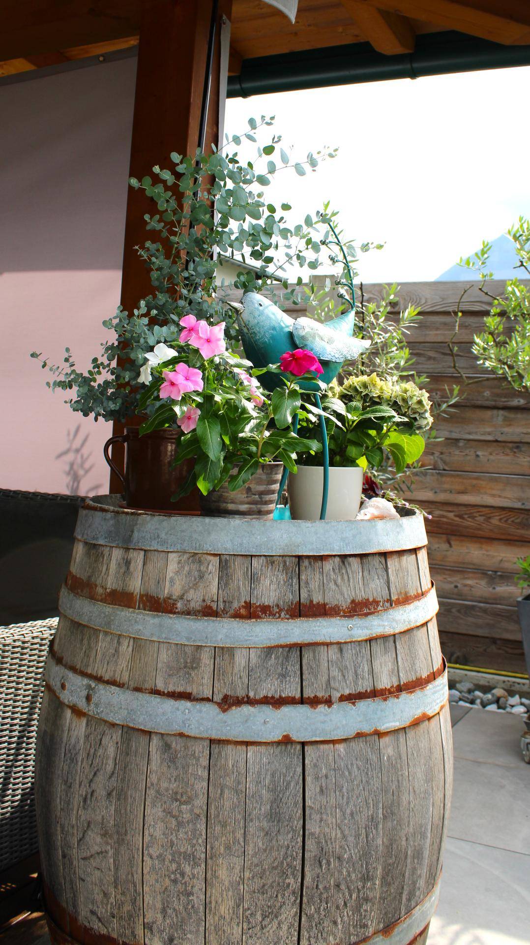 Dekoriertes Weinfass mit bunten Blumen auf einer sonnigen Terrasse.