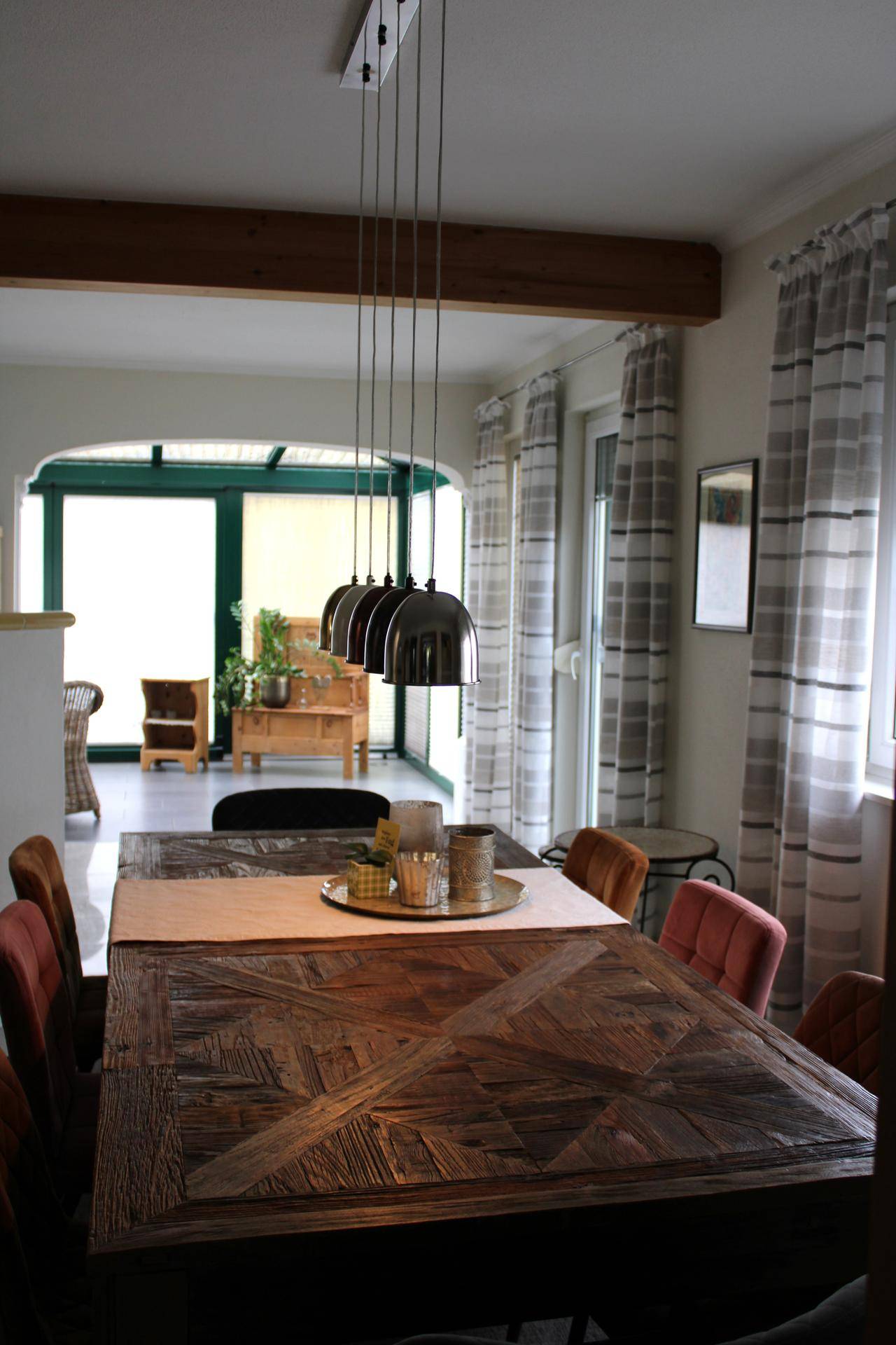 Esszimmer mit Holztisch, modernen Pendelleuchten und Blick in den Wintergarten.