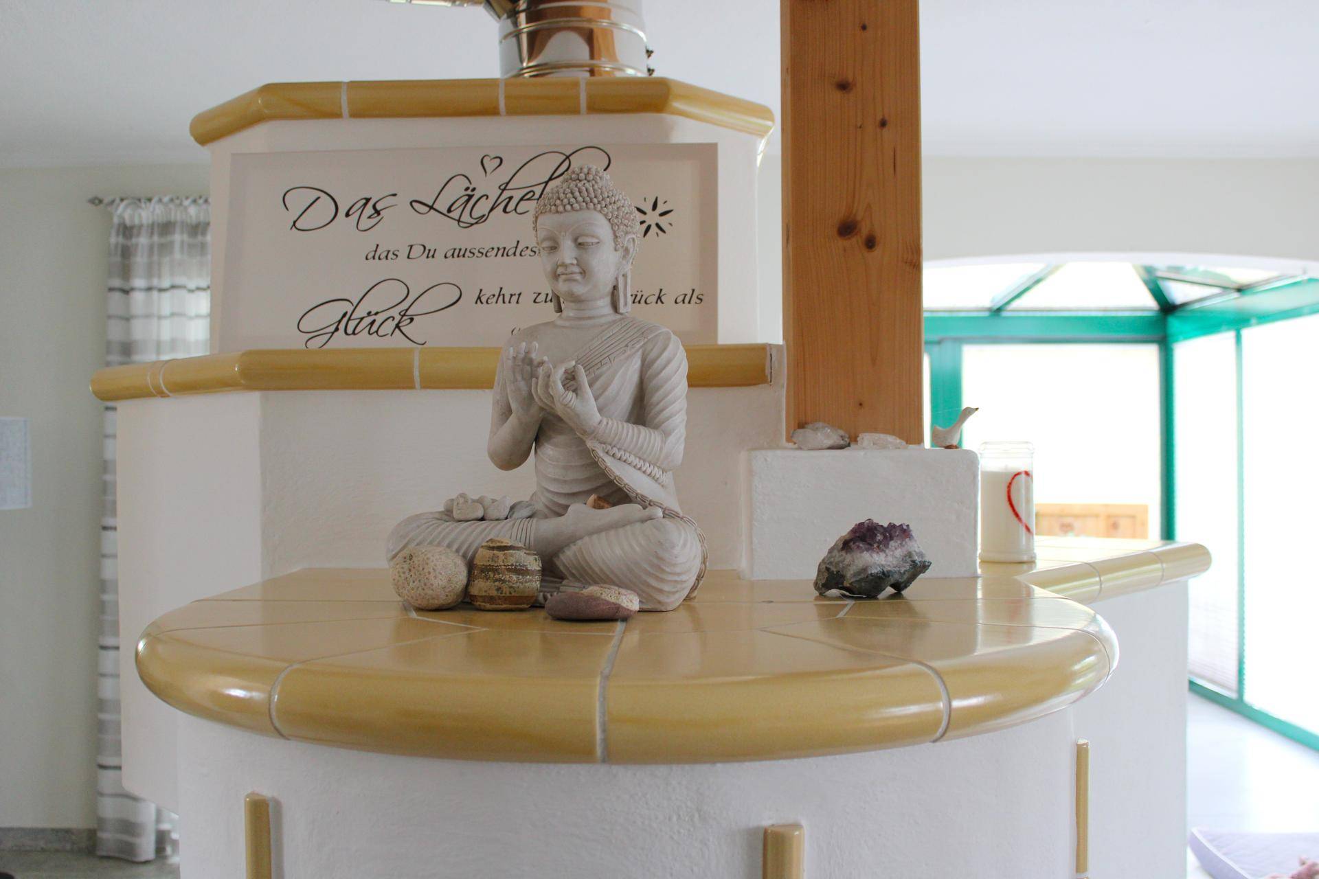 Detailansicht eines traditionellen Kachelofens mit Buddha-Statue und Dekoration.