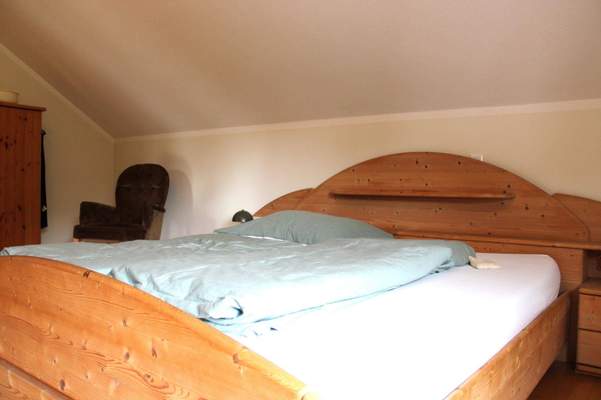 Gemütliches Schlafzimmer mit Holzbett, Dachschräge und natürlichem Lichteinfall.