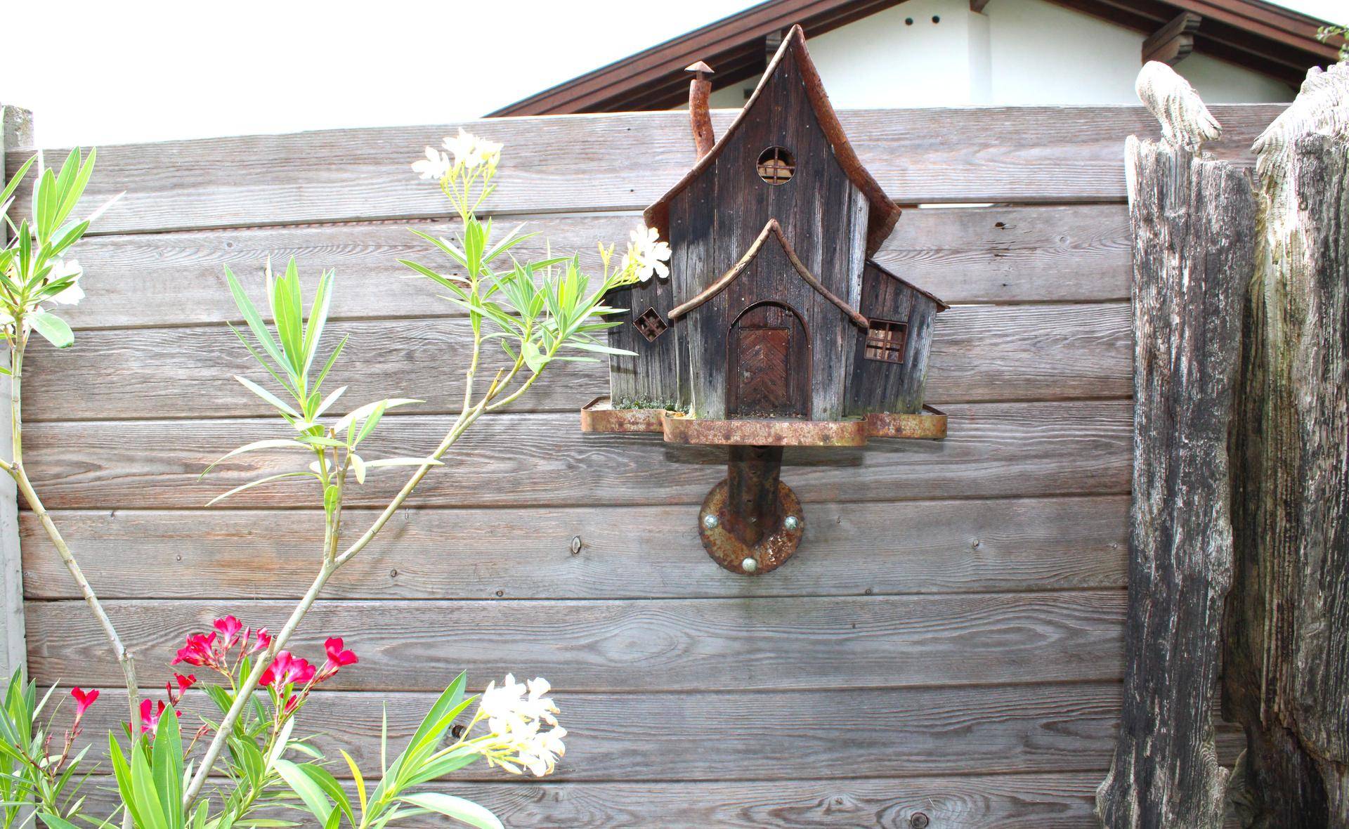 Rustikales Vogelhaus an einem Holzzaun im Gartenbereich.
