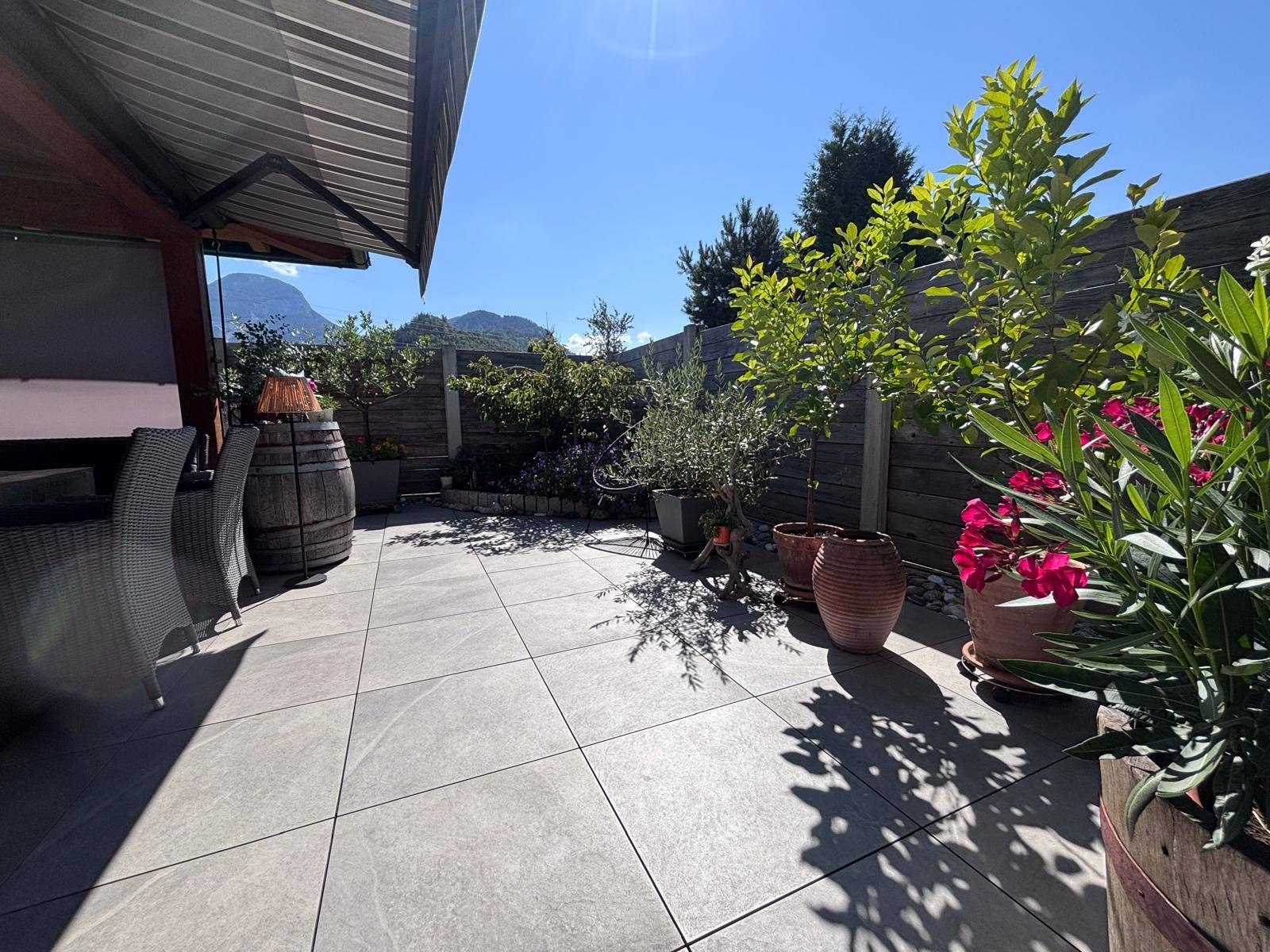 Sonniger Terrassenbereich mit großen Fliesen, Pflanzen und Blick auf die Berge.
