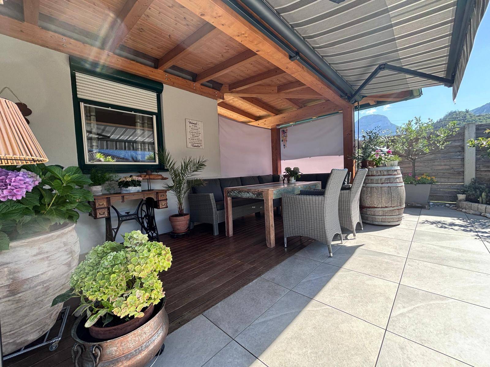 Überdachte Terrasse mit Holzboden, Sitzmöbeln und Blick auf die Berge.