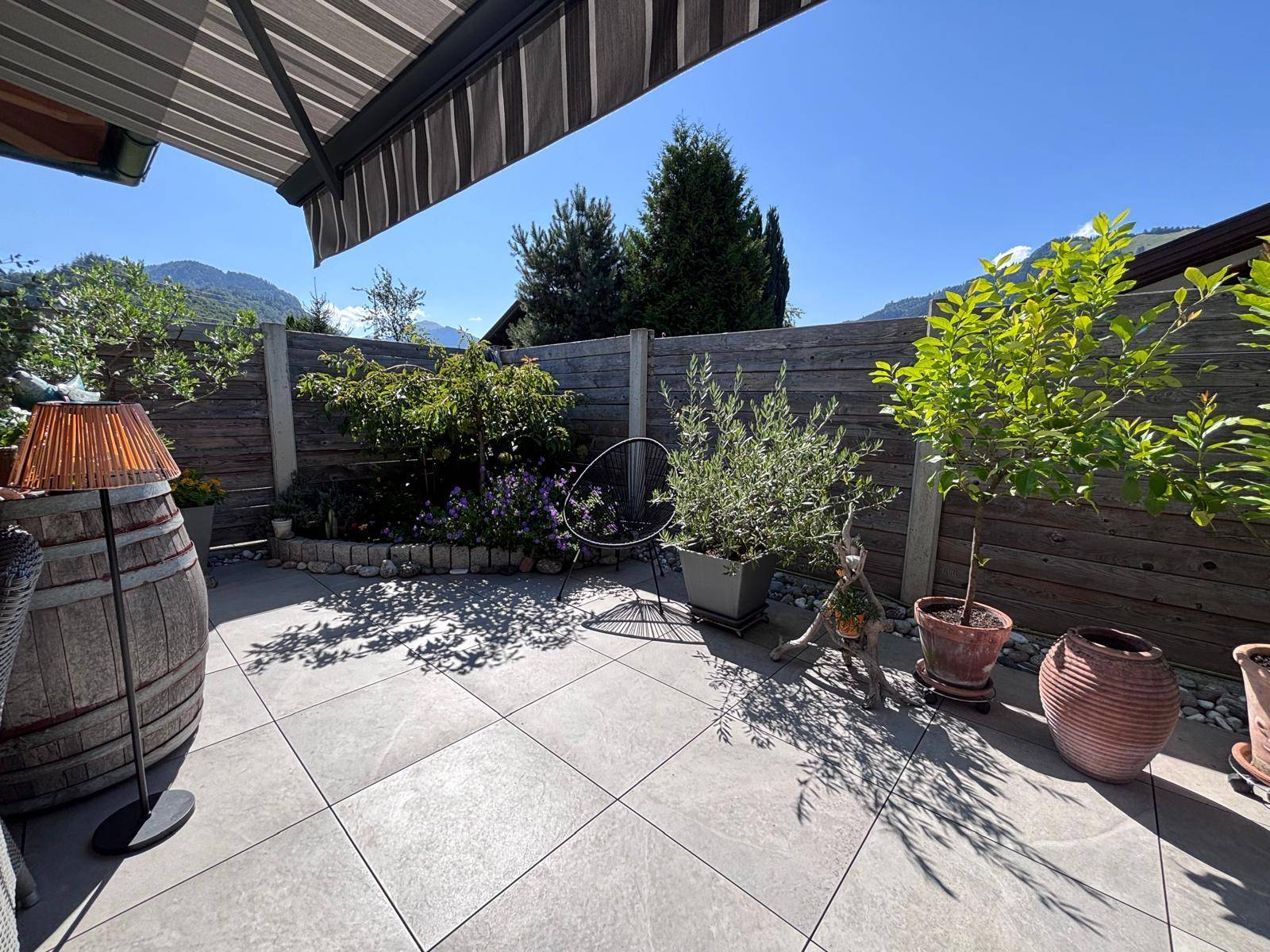 Geräumige Terrasse mit Fliesenboden, Pflanzen und Bergblick unter einer Markise.