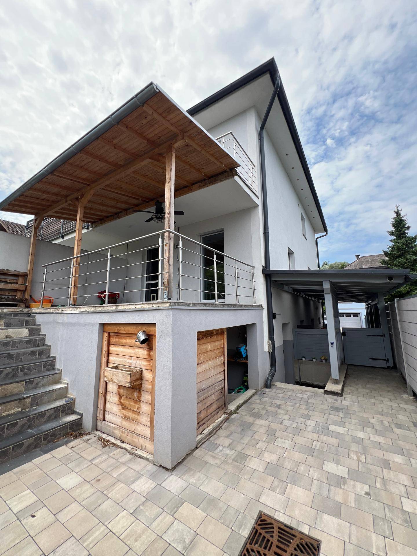 Modernes Haus mit überdachtem Balkon, Außentreppe und gepflastertem Einfahrtsbereich.