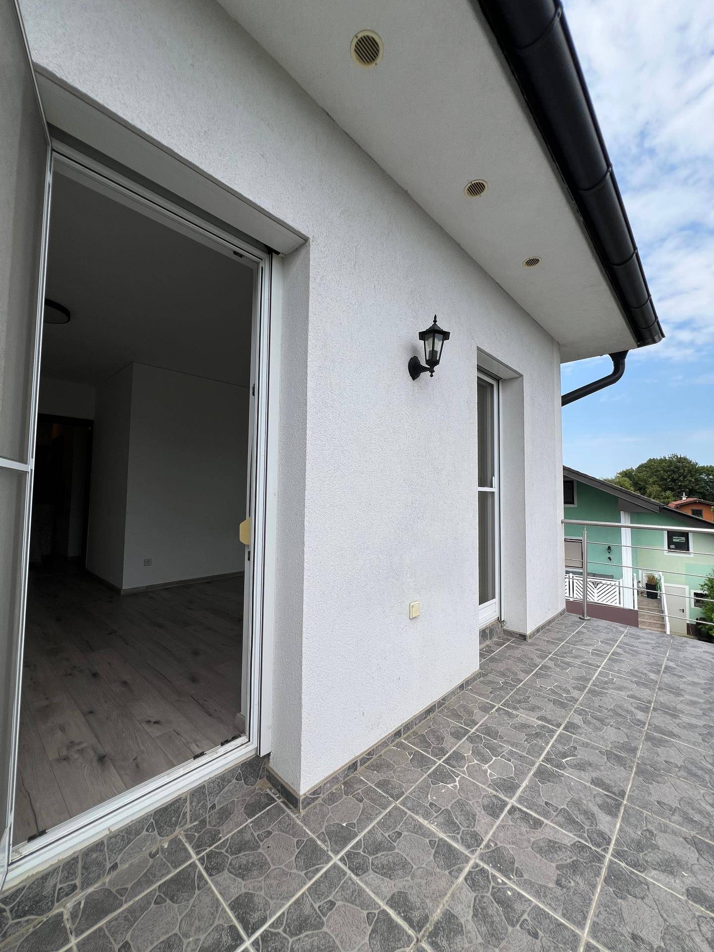 Balkon mit grauen Fliesen und Zugang zu einem Innenraum des Hauses.
